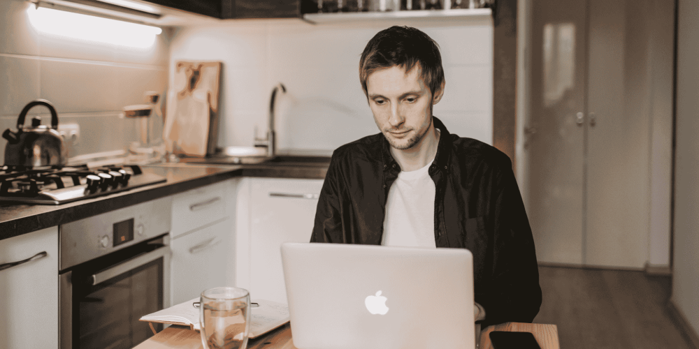 Entrepreneur travaillant sur un ordinateur portable à la maison, avec une tasse sur la table, analysant ses chiffres.
